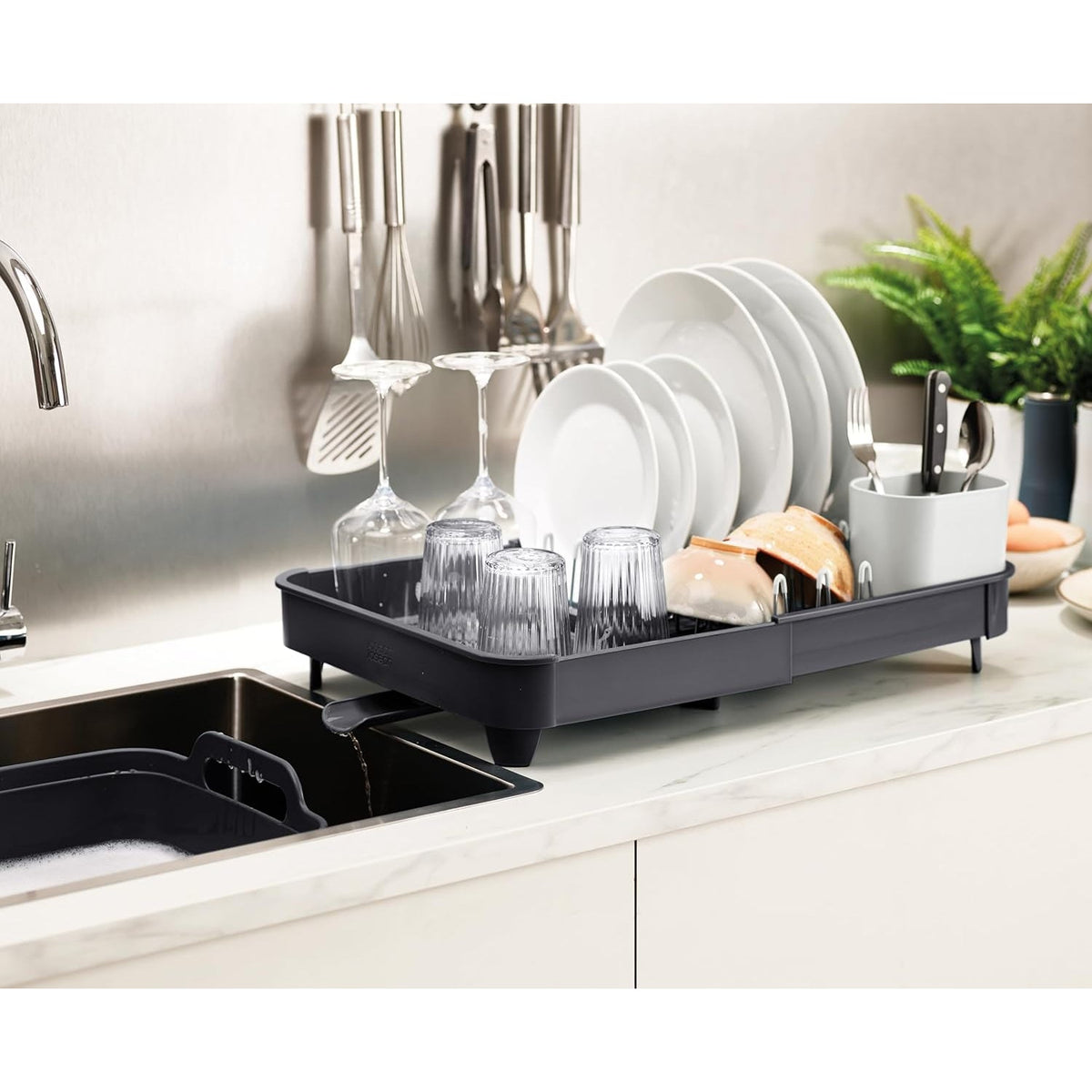 Escurridor de platos expandible gris oscuro con drenaje, lleno de vajilla, junto a un fregadero de cocina