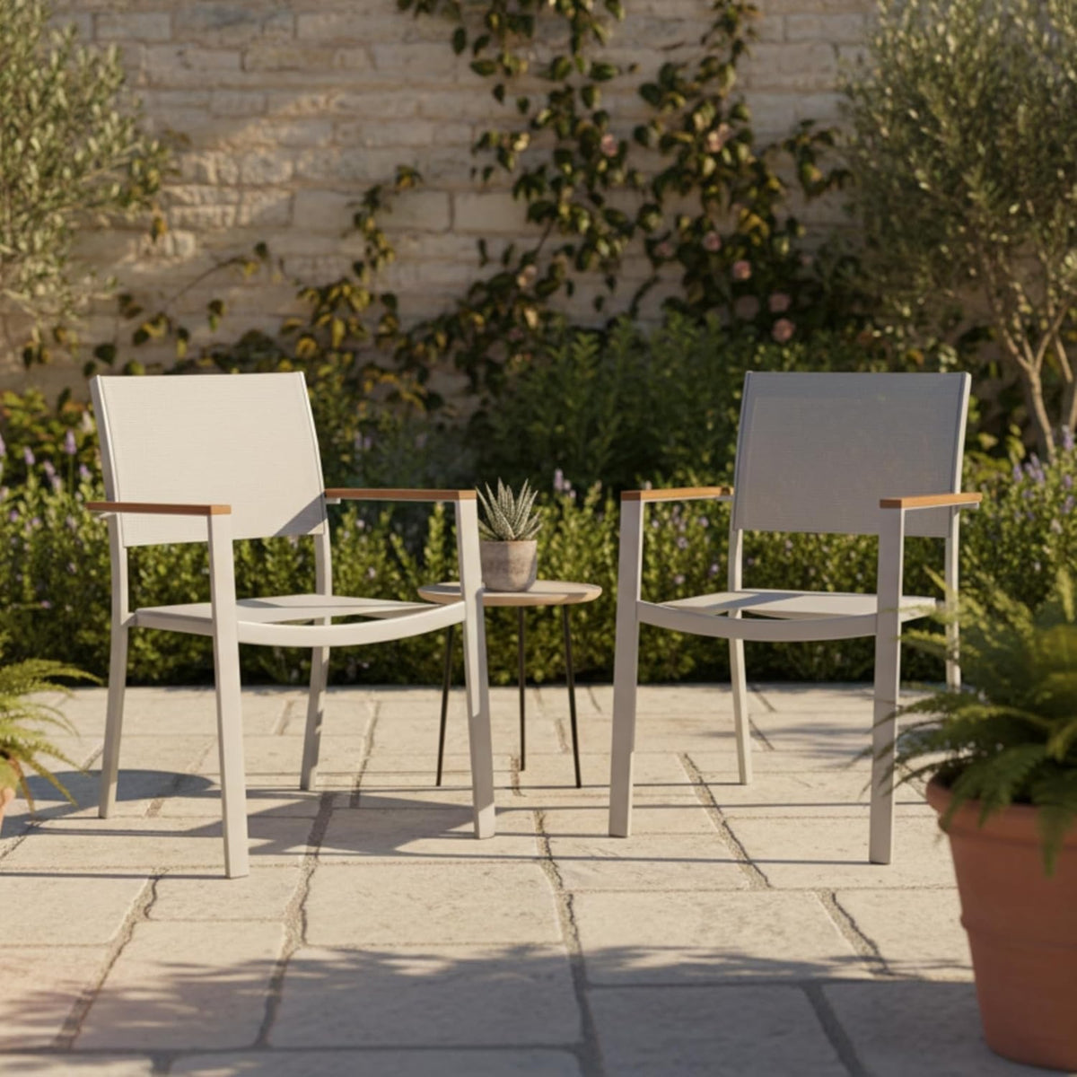 Dos sillas Tagula de metal gris con reposabrazos de madera, ambientadas en una terraza con plantas y pared de piedra